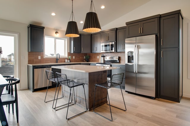 kitchen with a kitchen island, decorative light fixtures, light hardwood / wood-style flooring, stainless steel appliances, and vaulted ceiling