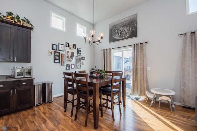 dining area featuring wood-type flooring, an inviting chandelier, and a high ceiling