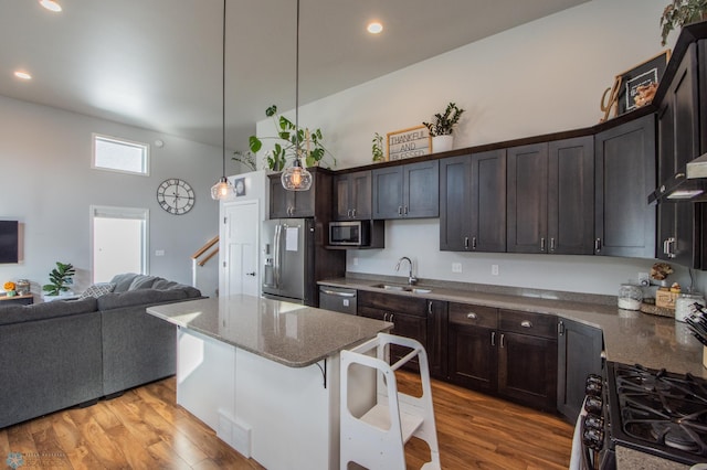 kitchen with light hardwood / wood-style floors, a center island, sink, appliances with stainless steel finishes, and decorative light fixtures