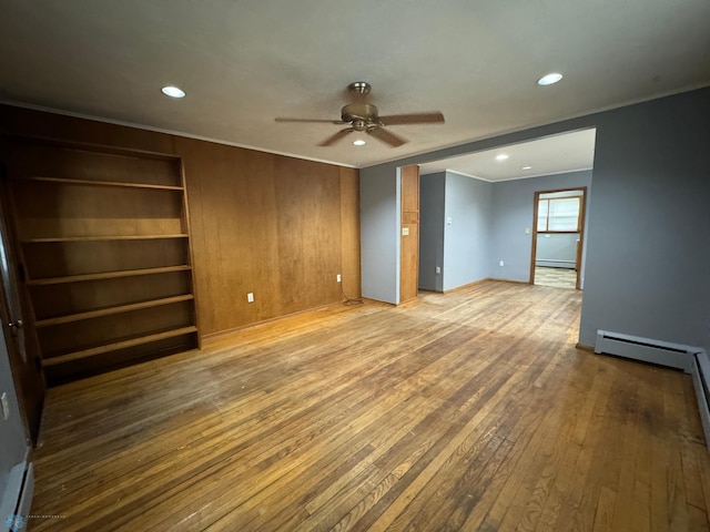 unfurnished room featuring a baseboard heating unit, light hardwood / wood-style floors, ceiling fan, and wood walls