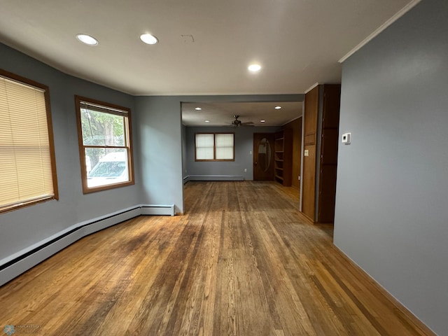 empty room with a baseboard heating unit, wood-type flooring, ceiling fan, and crown molding