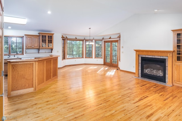 unfurnished living room featuring an inviting chandelier, light wood-type flooring, vaulted ceiling, and a tiled fireplace