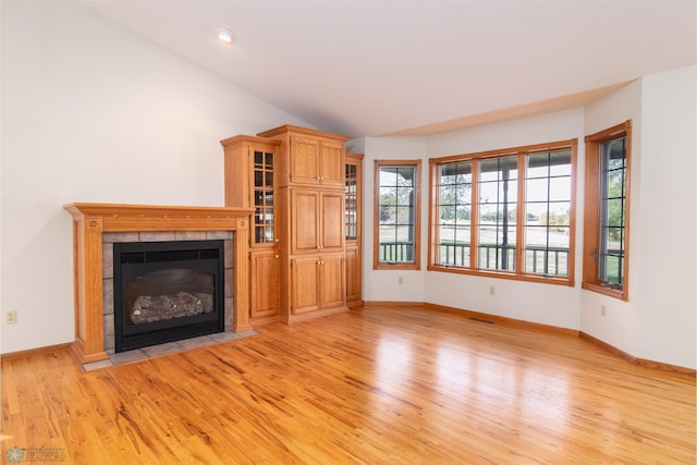 unfurnished living room featuring lofted ceiling, a tile fireplace, and light hardwood / wood-style flooring