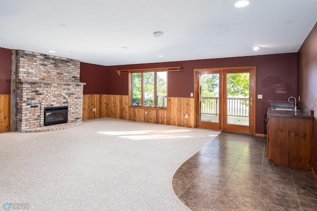 carpeted living room featuring a brick fireplace, wood walls, and sink