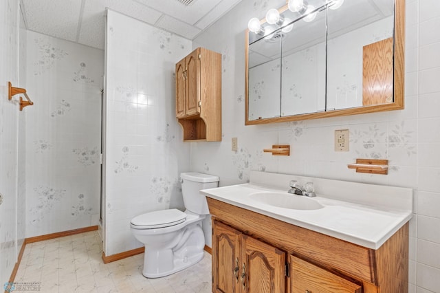 bathroom with tile walls, vanity, a paneled ceiling, toilet, and an enclosed shower