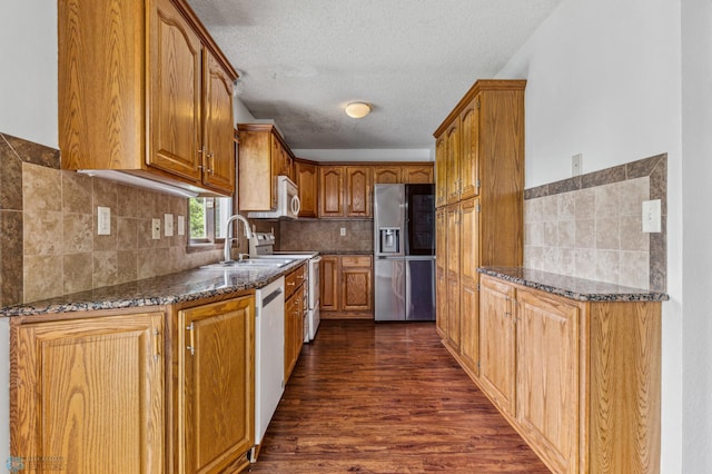 kitchen with dark stone counters, white appliances, dark hardwood / wood-style flooring, and sink