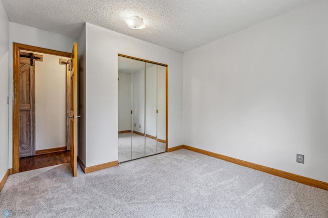 unfurnished bedroom with a closet, a textured ceiling, carpet floors, and a barn door