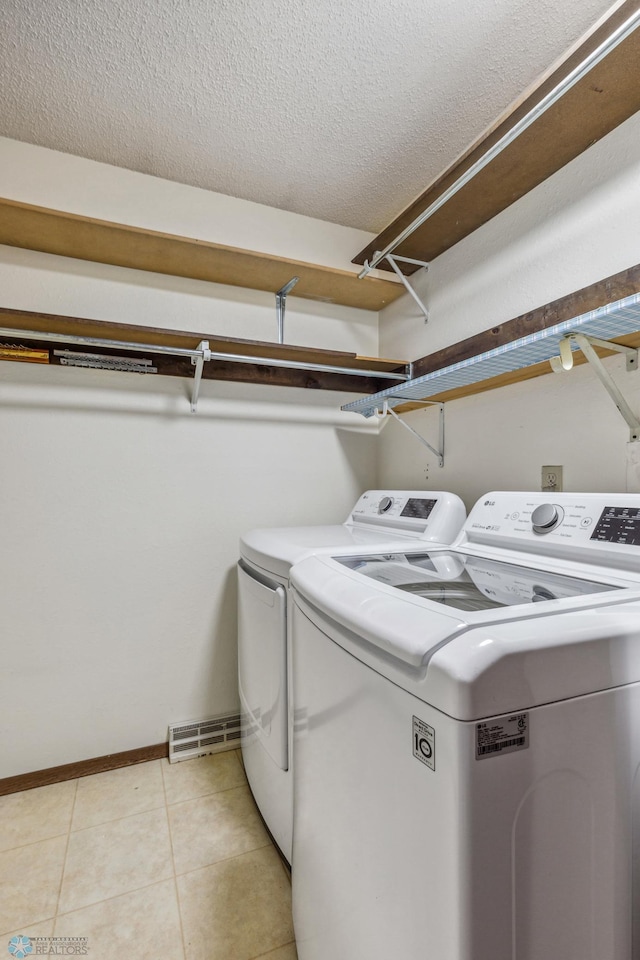 washroom with a textured ceiling, separate washer and dryer, and light tile patterned flooring