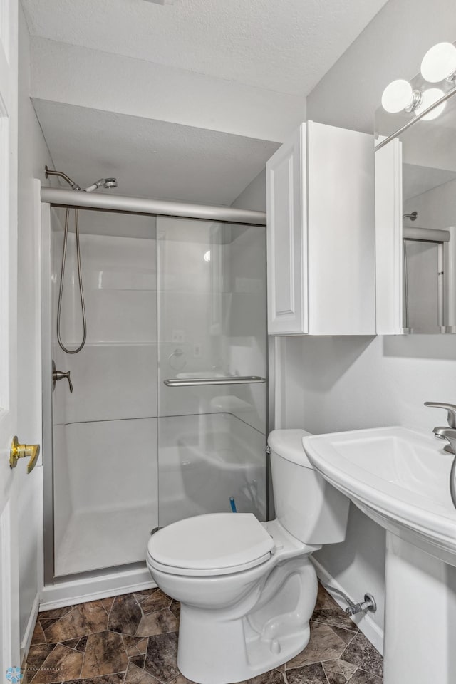 bathroom with a textured ceiling, toilet, sink, and an enclosed shower