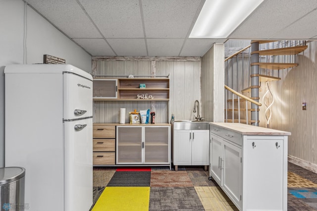 kitchen with a drop ceiling, white cabinets, white refrigerator, and wooden walls