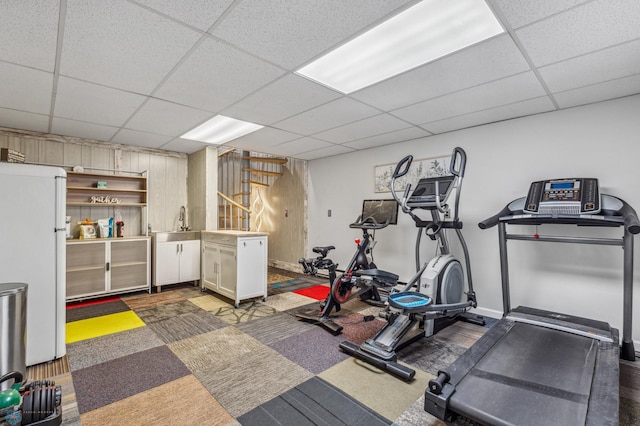 exercise room with a drop ceiling, dark carpet, and sink