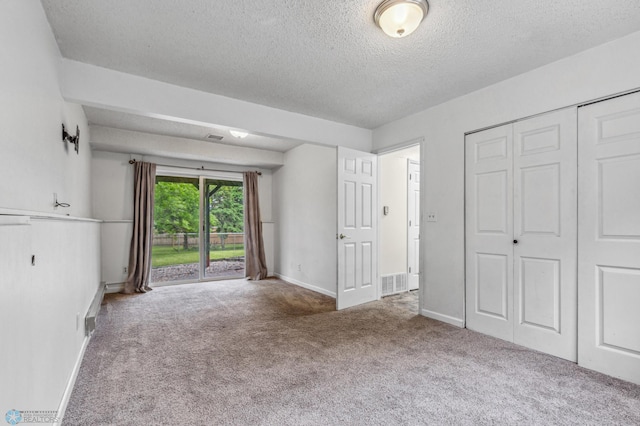 unfurnished bedroom with a closet, a textured ceiling, carpet floors, and access to outside