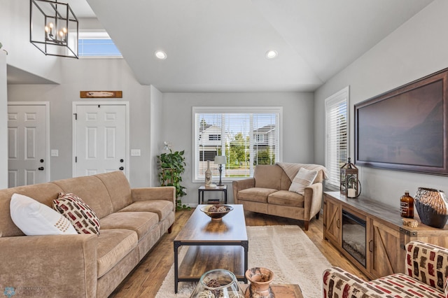 living room with a notable chandelier, light hardwood / wood-style flooring, vaulted ceiling, and a healthy amount of sunlight