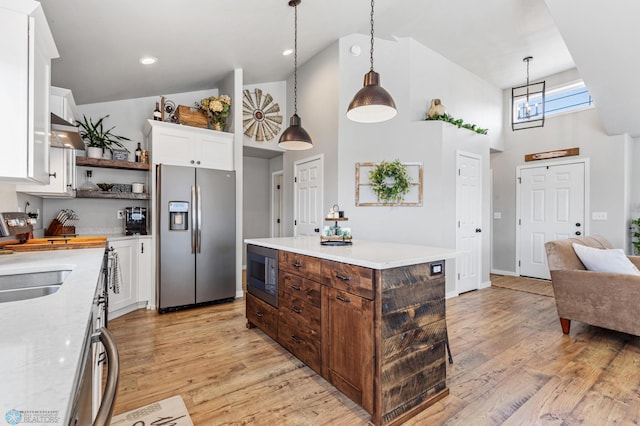 kitchen with black microwave, white cabinets, a kitchen island, high vaulted ceiling, and stainless steel fridge