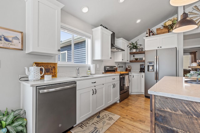 kitchen featuring appliances with stainless steel finishes, white cabinetry, wall chimney exhaust hood, lofted ceiling, and sink