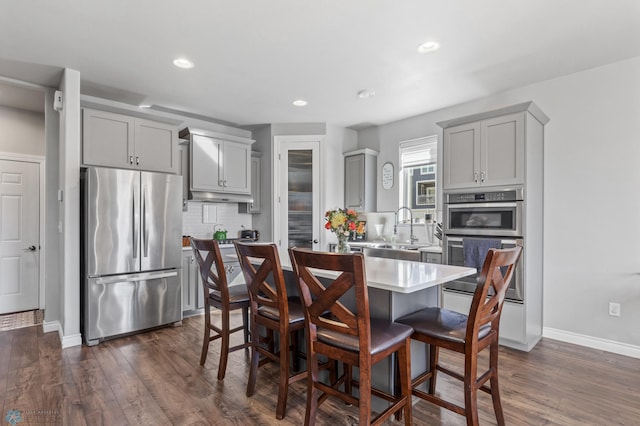 kitchen with gray cabinets, dark wood-type flooring, a kitchen bar, a kitchen island, and appliances with stainless steel finishes