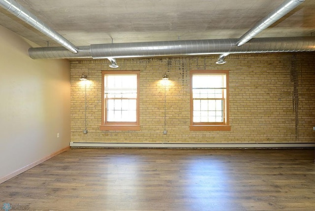 unfurnished room with hardwood / wood-style floors, baseboard heating, brick wall, and a healthy amount of sunlight