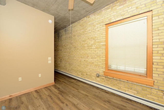 spare room featuring brick wall, ceiling fan, baseboard heating, and hardwood / wood-style flooring