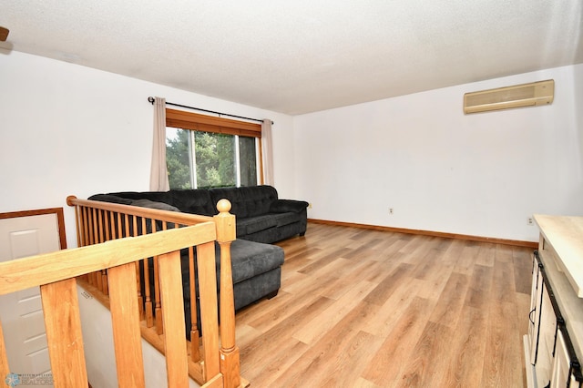 living room featuring light wood-type flooring, a textured ceiling, and a wall mounted air conditioner