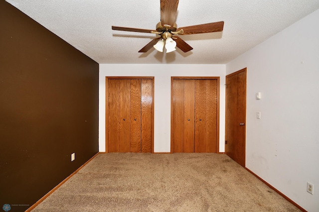 unfurnished bedroom featuring two closets, carpet, ceiling fan, and a textured ceiling