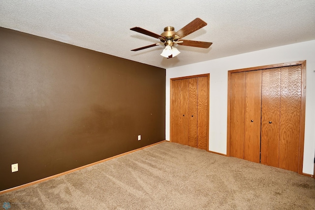 unfurnished bedroom with ceiling fan, multiple closets, a textured ceiling, and carpet flooring