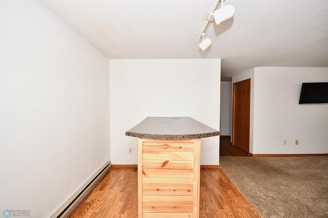 kitchen with a baseboard radiator, a textured ceiling, light brown cabinets, and hardwood / wood-style flooring