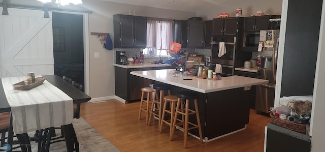 kitchen featuring hardwood / wood-style flooring, a kitchen island, a barn door, a kitchen breakfast bar, and appliances with stainless steel finishes