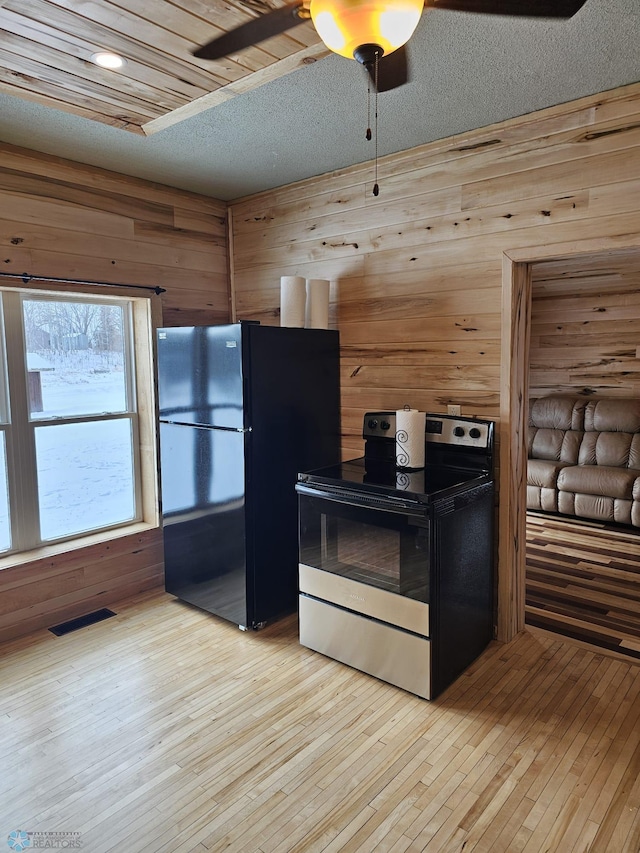 kitchen featuring stainless steel appliances, wood walls, and light hardwood / wood-style flooring