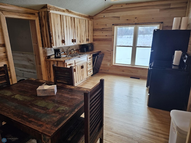 kitchen with light wood-type flooring, a textured ceiling, lofted ceiling, wooden walls, and black appliances