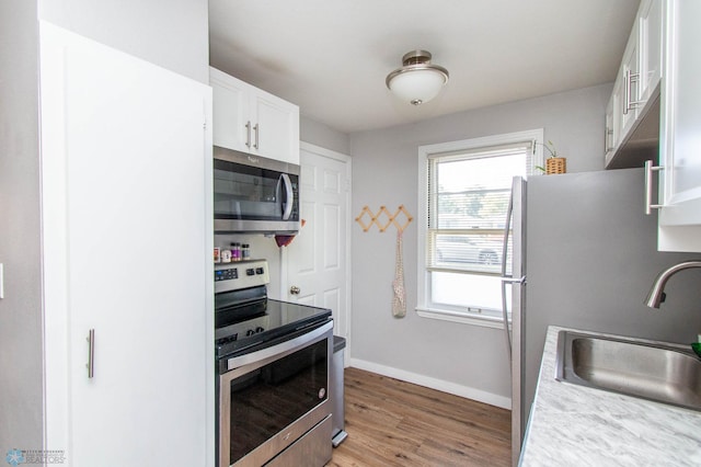 kitchen featuring appliances with stainless steel finishes, white cabinets, light stone countertops, light hardwood / wood-style flooring, and sink