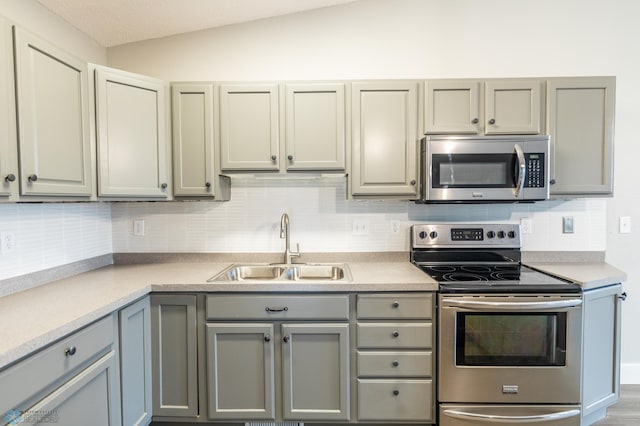 kitchen featuring tasteful backsplash, sink, lofted ceiling, gray cabinetry, and stainless steel appliances