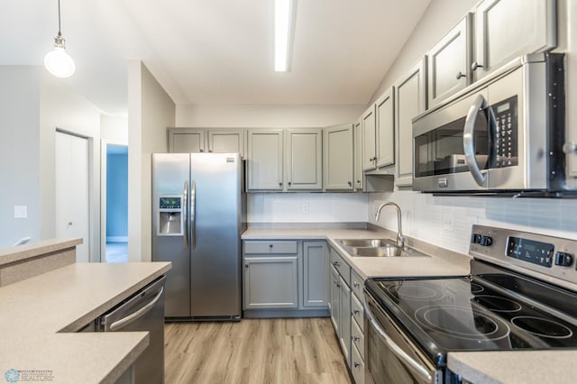 kitchen with tasteful backsplash, sink, light hardwood / wood-style flooring, appliances with stainless steel finishes, and decorative light fixtures