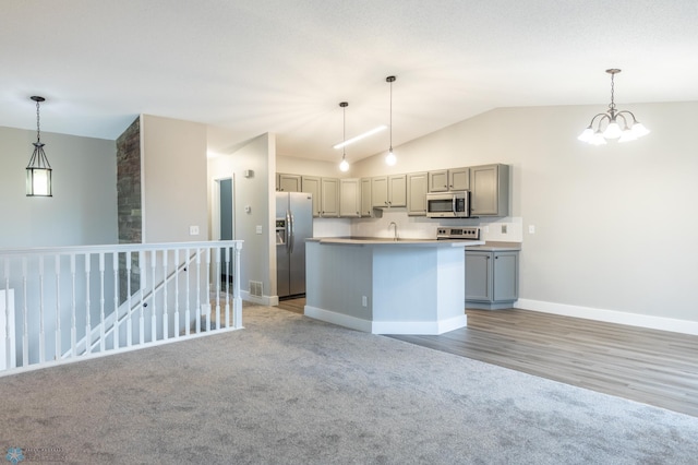 kitchen with hanging light fixtures, gray cabinetry, vaulted ceiling, stainless steel appliances, and a center island with sink