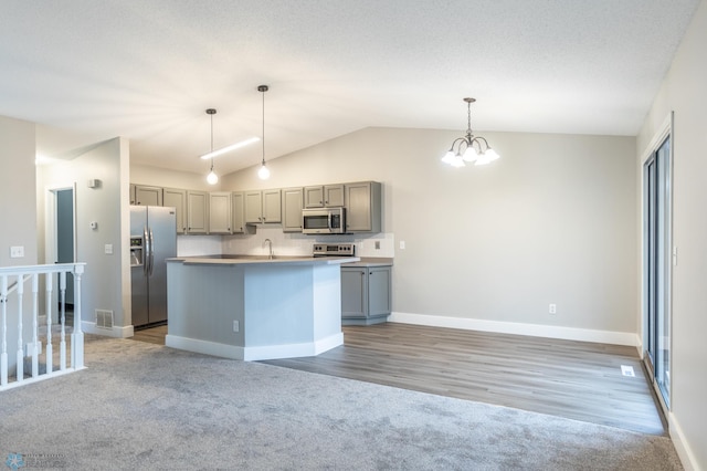 kitchen with an island with sink, lofted ceiling, gray cabinetry, stainless steel appliances, and decorative light fixtures