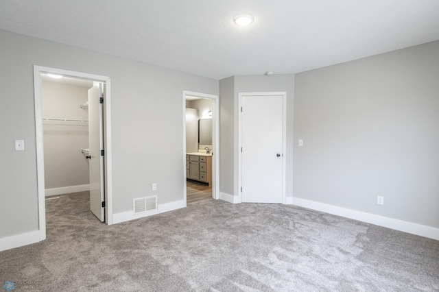 unfurnished bedroom featuring light colored carpet, a closet, sink, and a walk in closet