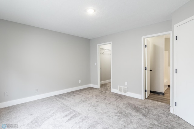 unfurnished bedroom with a spacious closet, a closet, and light carpet