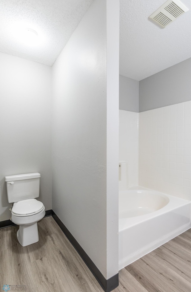 bathroom with wood-type flooring, a tub to relax in, a textured ceiling, and toilet