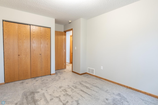 unfurnished bedroom featuring light colored carpet, a textured ceiling, and a closet