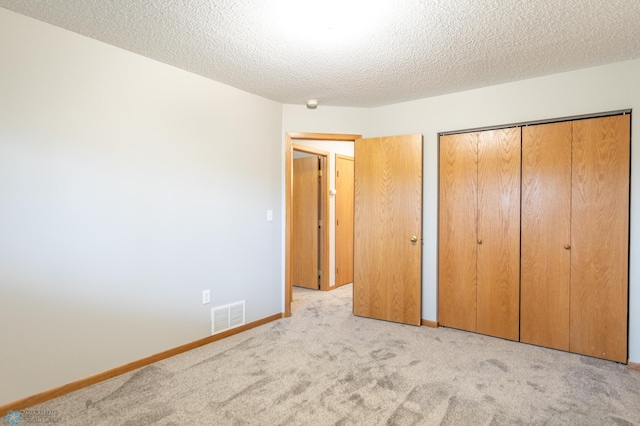 unfurnished bedroom featuring a textured ceiling, light carpet, and a closet