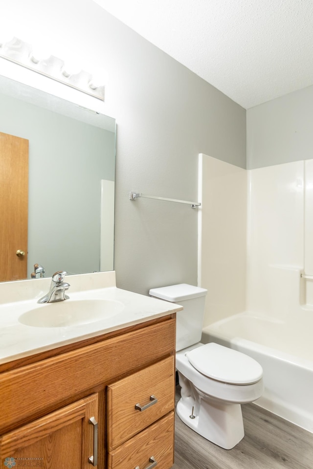 full bathroom featuring a textured ceiling, tub / shower combination, hardwood / wood-style floors, vanity, and toilet