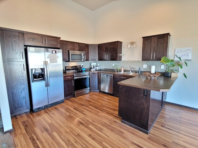 kitchen with dark brown cabinetry, appliances with stainless steel finishes, kitchen peninsula, and light hardwood / wood-style flooring