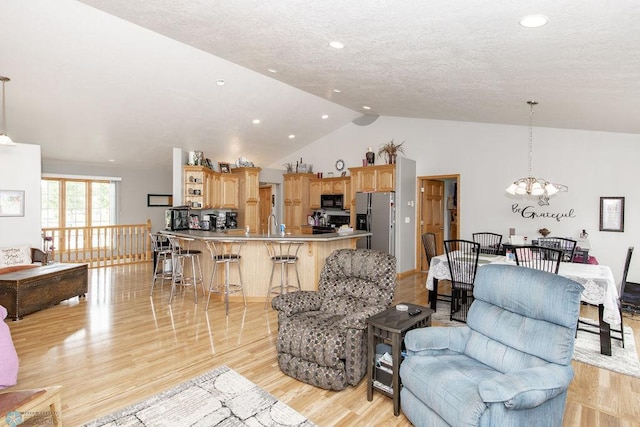 living room with a textured ceiling, light hardwood / wood-style floors, vaulted ceiling, and an inviting chandelier