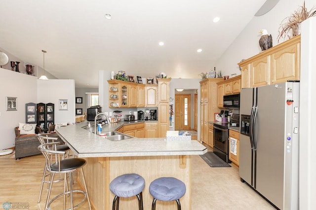 kitchen featuring sink, vaulted ceiling, kitchen peninsula, a kitchen bar, and black appliances