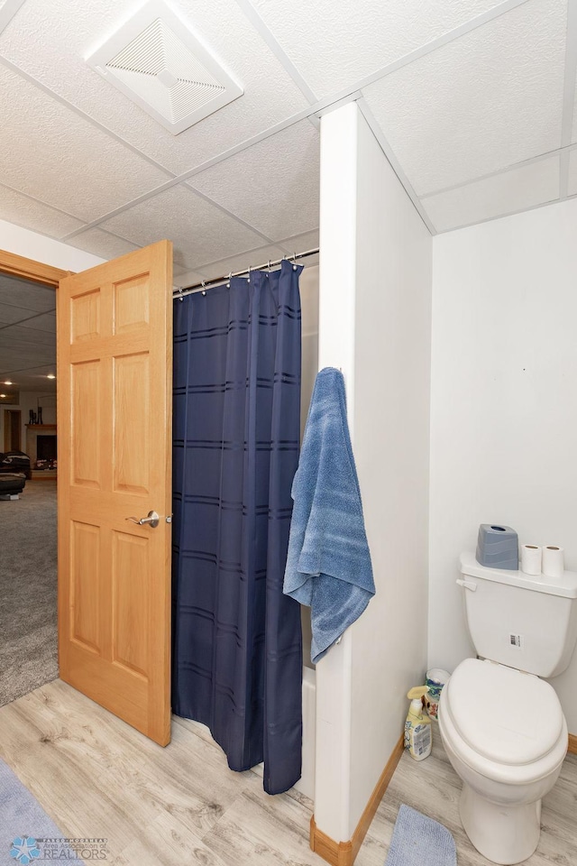 bathroom featuring toilet, hardwood / wood-style floors, a shower with shower curtain, and a drop ceiling