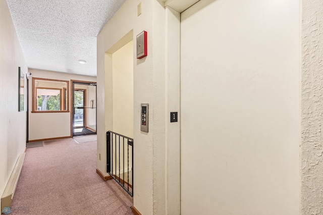 hall featuring elevator, a textured ceiling, and light colored carpet