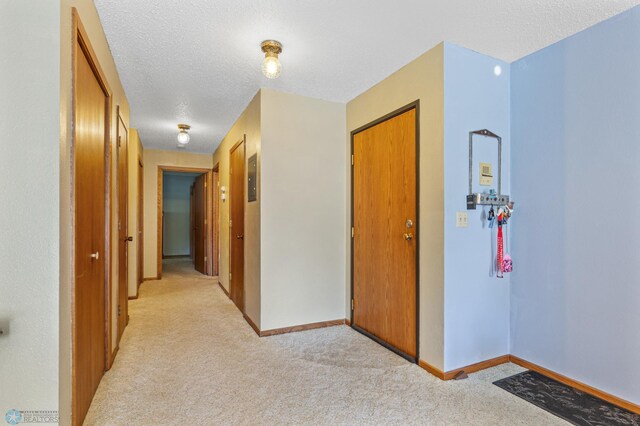 hall with light colored carpet and a textured ceiling