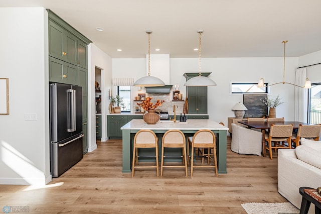 kitchen with an island with sink, decorative light fixtures, light hardwood / wood-style flooring, green cabinets, and high end refrigerator