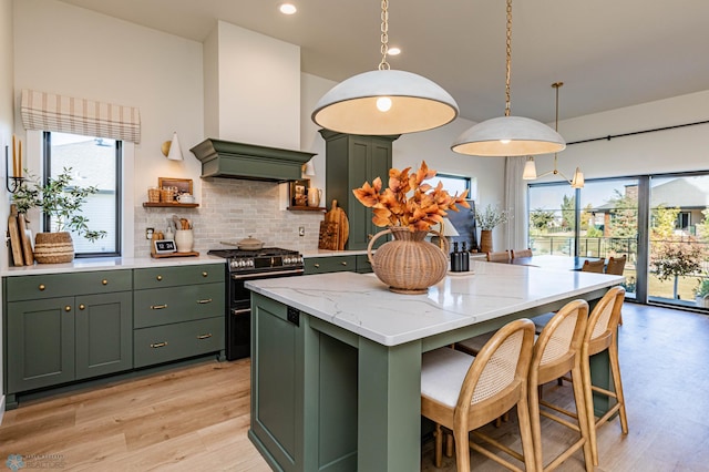 kitchen with gas range oven, decorative light fixtures, custom range hood, and a healthy amount of sunlight