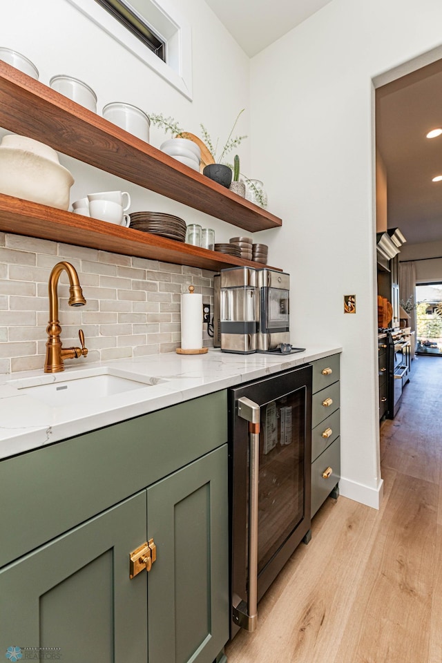 bar with light stone counters, wine cooler, sink, light hardwood / wood-style flooring, and backsplash