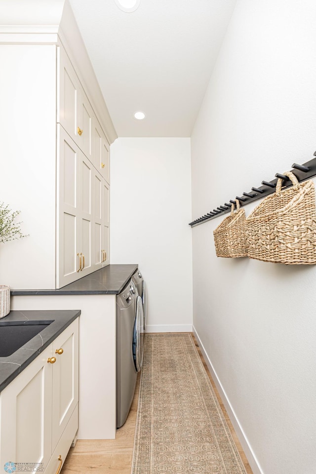 clothes washing area featuring washing machine and clothes dryer, light hardwood / wood-style floors, and cabinets